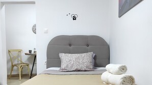Una cama bien hecha con una cubierta acolchada, un cabecero tapizado en gris y dos toallas enrolladas.