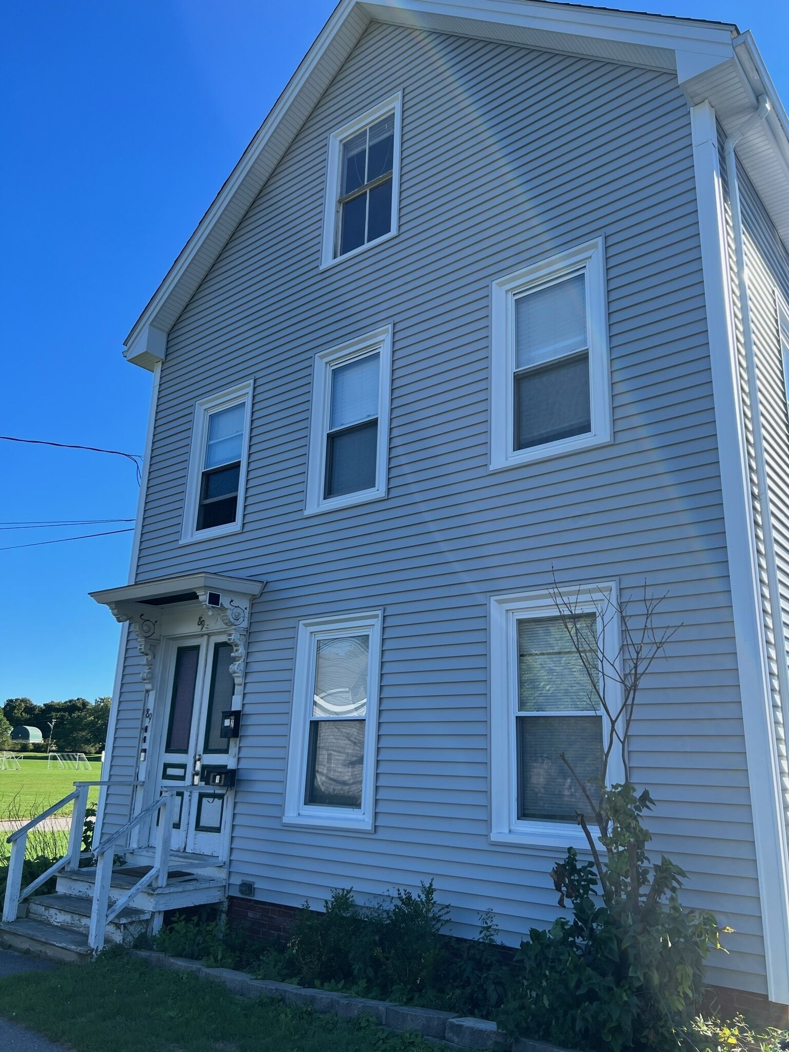 A two-story house with a front porch, multiple windows, and a small garden area.