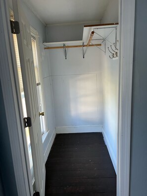 Una habitación estrecha con paredes blancas, piso de madera oscura y techo con una viga de madera.