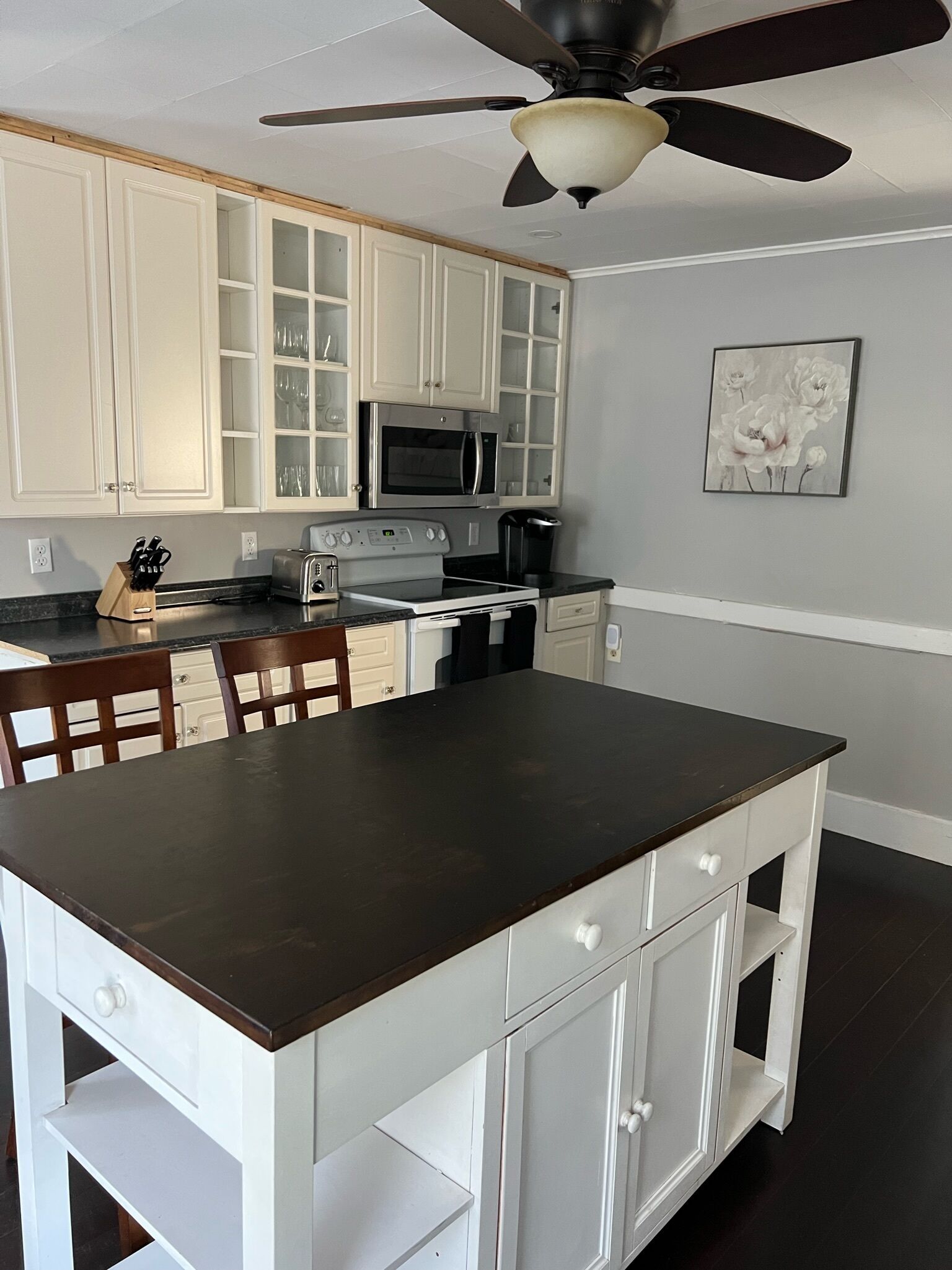 A kitchen with white cabinetry, a dark countertop island, a ceiling fan, and a microwave.