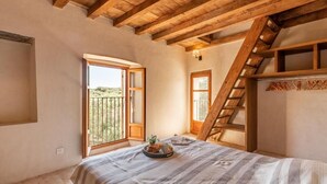 Een slaapkamer met een bed, een raam, een houten trap en een balkon.