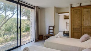 Een slaapkamer met twee bedden, een groot raam en uitzicht op bomen.