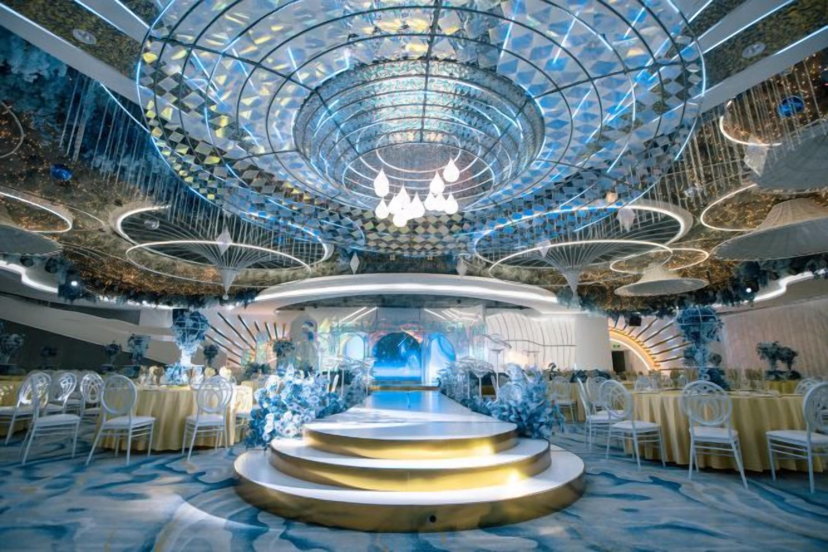 A grand hall with a central stage, tiered seating, and a decorative ceiling.