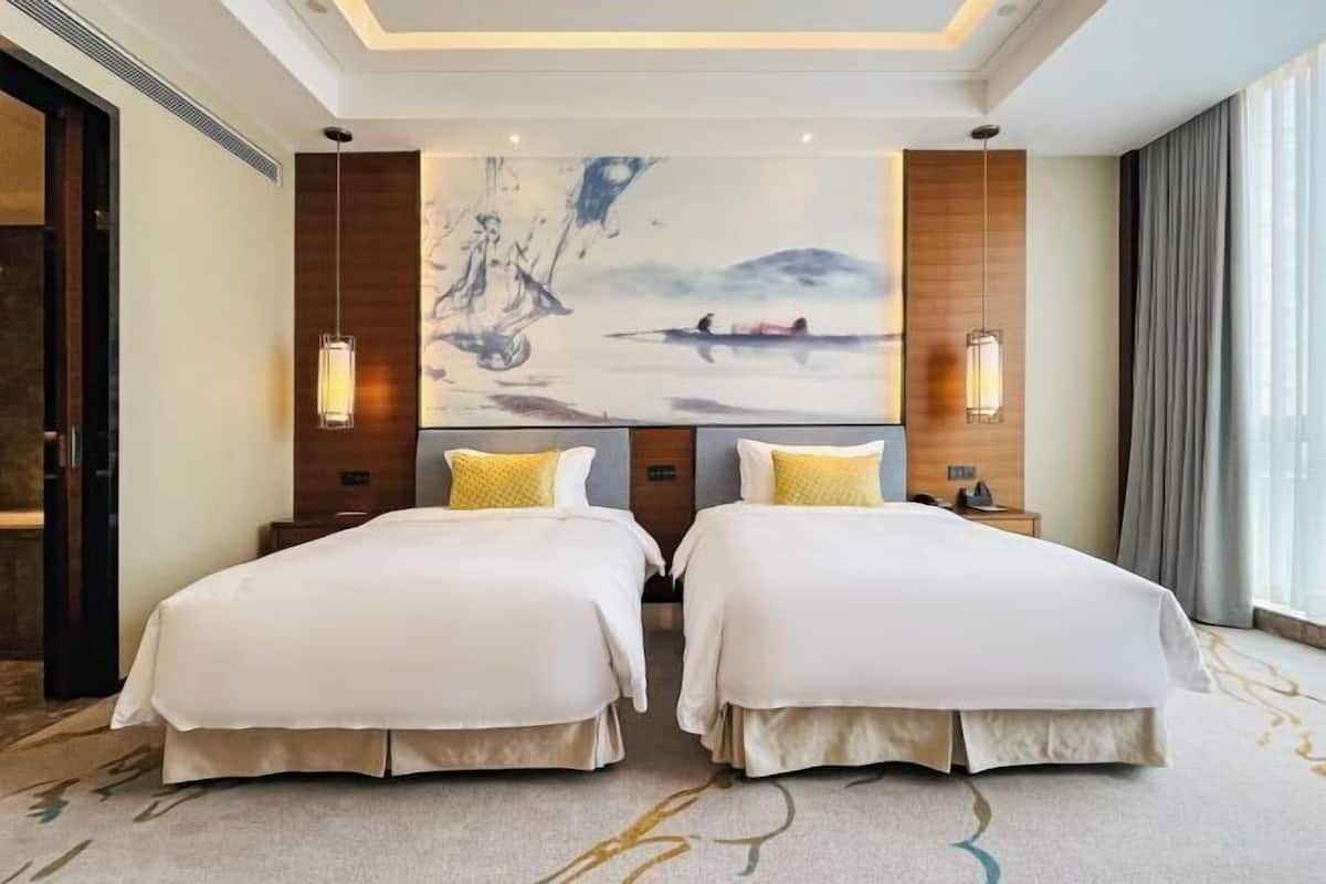 Une chambre d’hôtel avec deux lits, une grande peinture abstraite au mur et une vue sur l’extérieur.
