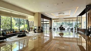 A spacious lobby with a reflective floor, a seating area with a sofa, and large windows offering a view of the outdoors.