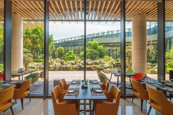 An indoor dining area with large windows, a view of a landscaped garden, and modern furniture. - Rong Qiao Hotel (Fuzhou)