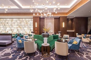 A hotel lobby with a modern design, featuring a mix of seating arrangements, a patterned carpet, and a large window with a view. - Rong Qiao Hotel (Fuzhou)