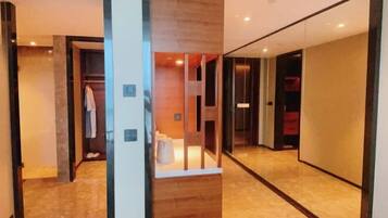 Un pasillo moderno de hotel con piso de madera, una partición de vidrio y una maleta roja visible al fondo.