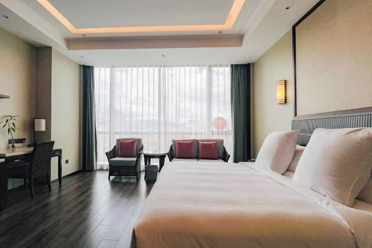 Une chambre d’hôtel avec un grand lit, un bureau, une chaise et une vue sur la ville grâce à de grandes fenêtres.