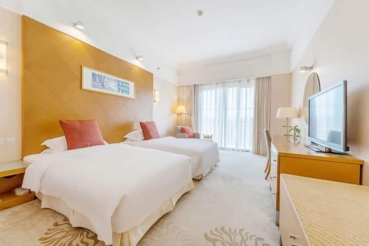 Une chambre d’hôtel avec deux lits, une télévision, un bureau et une grande fenêtre avec des rideaux.