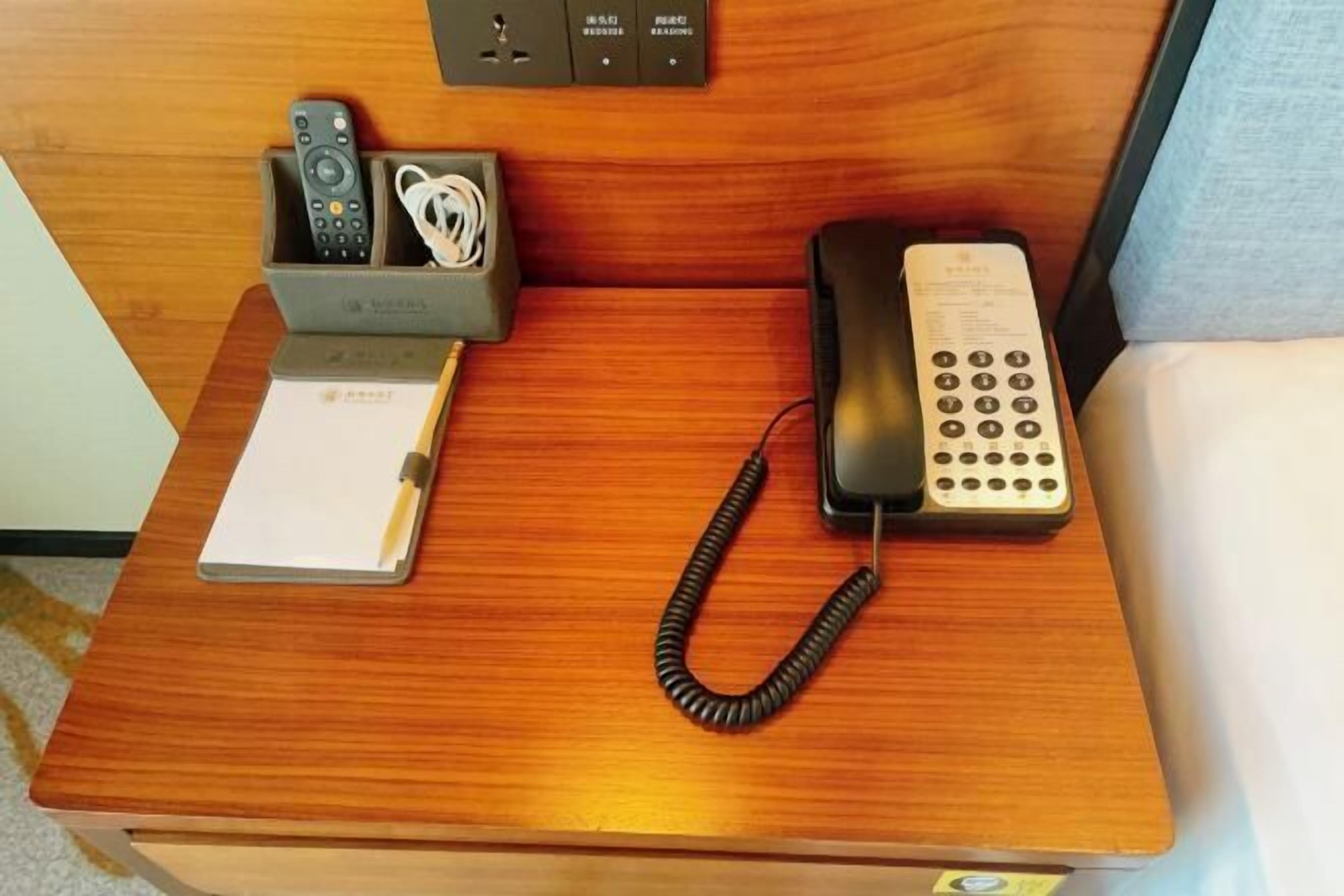 Uma escrivaninha de madeira com um telefone, um controle remoto e um bloco de notas.