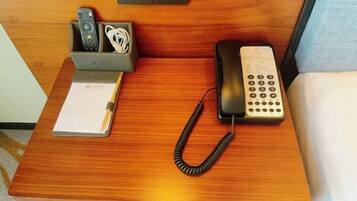 Uma escrivaninha de madeira com um telefone, um controle remoto e um bloco de notas.