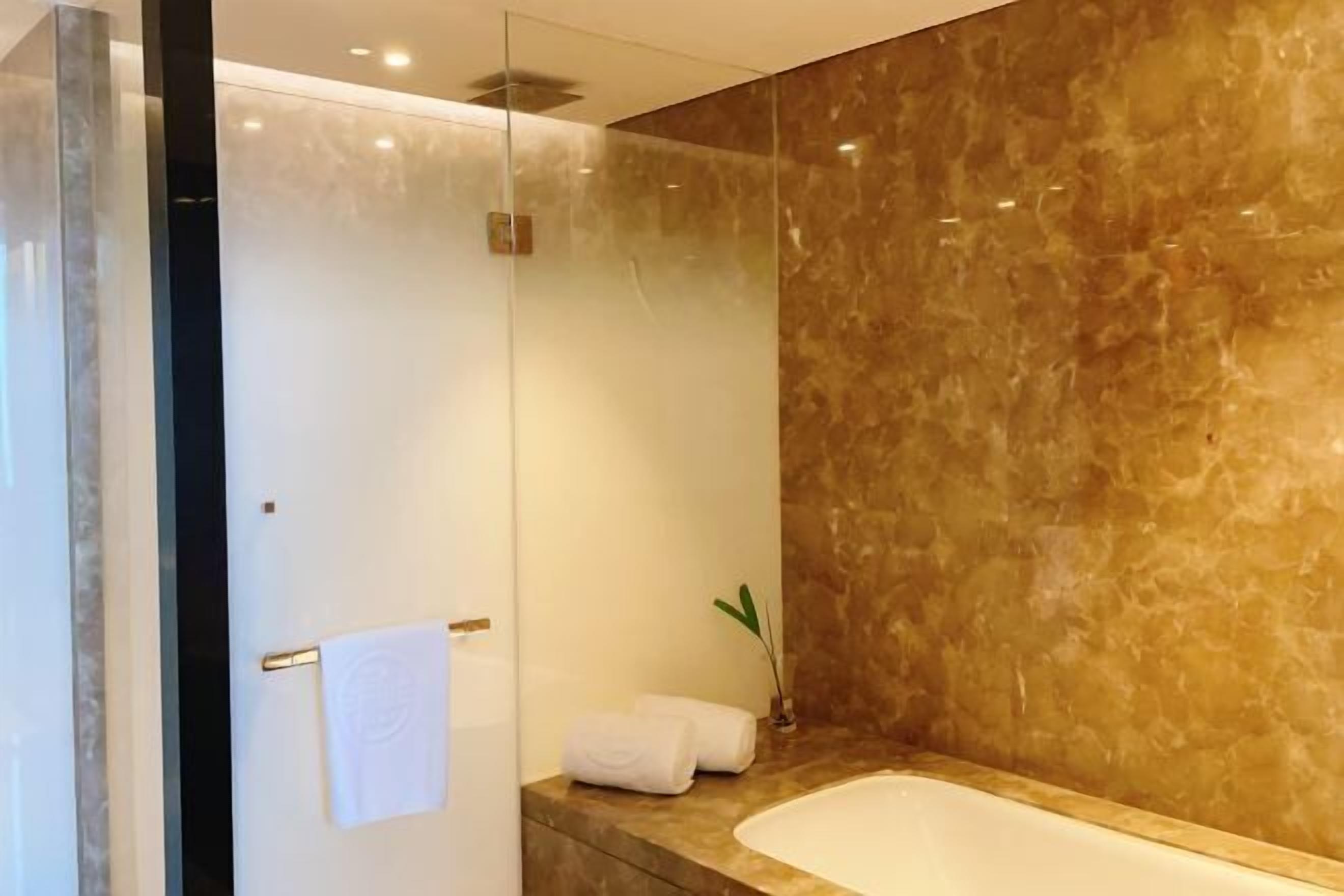 Ein modernes Badezimmer mit Duschkabine aus Glas, einer Badewanne mit Marmorplatte und einer kleinen Pflanze auf dem Waschtisch.