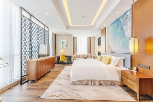 A modern hotel room with a large bed, a wooden headboard, a bedside table, a TV, and a large window.