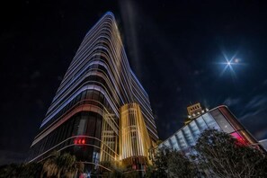 A tall, modern building with a curved facade and illuminated windows at night.