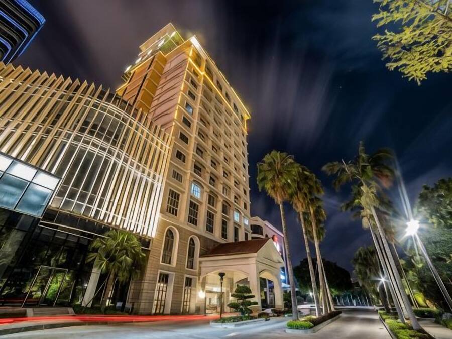 Un hotel de varios pisos con fachada de vidrio curva, palmeras y una calle bien iluminada.