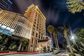 A multi-story hotel with a curved facade, palm trees, and a well-lit street.