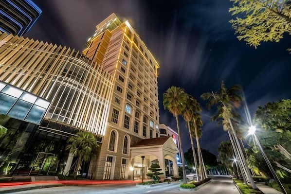 A multi-story hotel with a curved facade, palm trees, and a well-lit street.