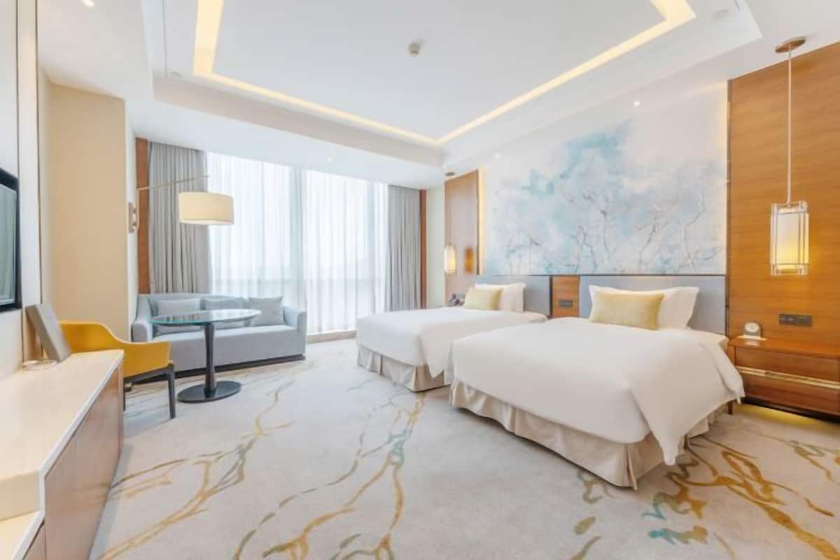 Une chambre d’hôtel avec deux lits, un canapé, un bureau et une grande fenêtre.