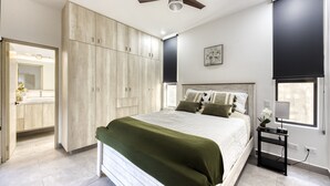 Un dormitorio con cama, mesita de noche, ventilador de techo, ventana con persianas y armario.