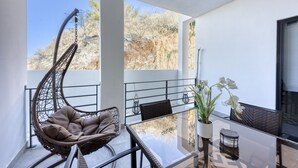 Un balcón con una silla colgante, una mesa de vidrio y plantas en macetas.