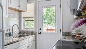 A compact kitchen with white cabinetry, a built-in dishwasher, a window with a view of greenery, and a small window above the sink.