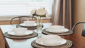 A dining table with white plates and bowls, a vase with white flowers, and woven placemats.
