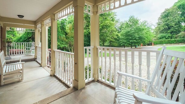 A covered porch with white railings, benches, and a view of a landscaped garden.
