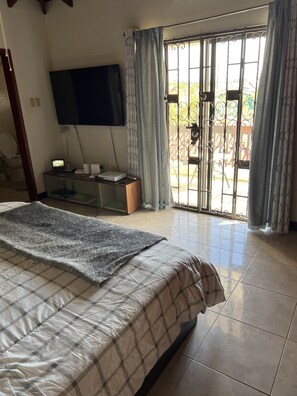 A bedroom with a bed, a TV mounted on the wall, a desk with a computer, and a sliding glass door leading to an outdoor area. - Free loaner car…Paradise get away near beach. (Saint James)