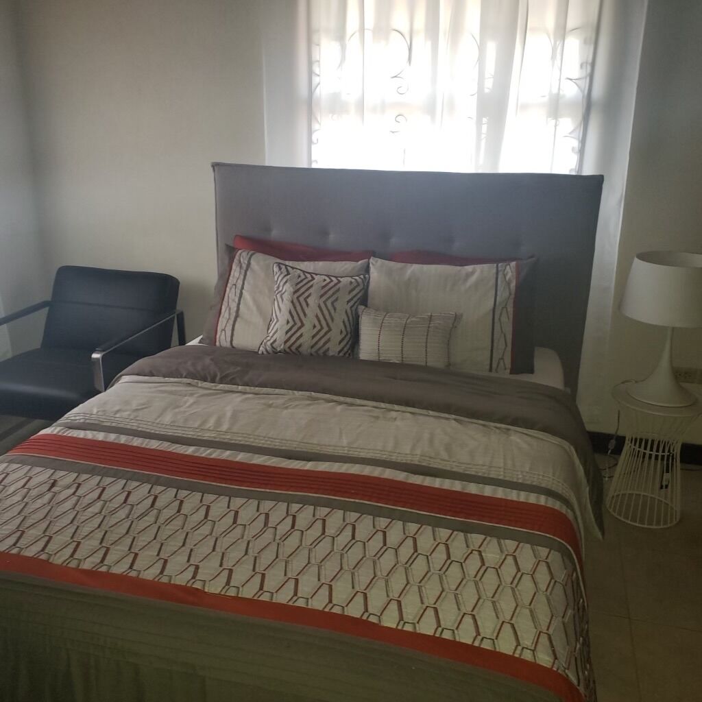 A hotel room with a bed, a chair, a lamp, and a window with curtains.