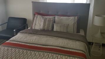 A hotel room with a bed, a chair, a lamp, and a window with curtains.