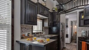 A modern kitchen with dark cabinetry, a central island with breakfast items, and a staircase leading to an upper level.