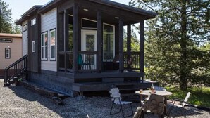 A small cabin with a porch, a gravel driveway, and outdoor seating.