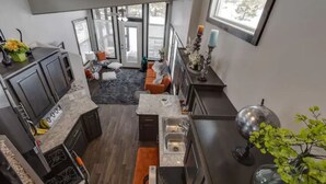 A modern kitchen with dark cabinetry, a granite countertop, and a built-in oven. There is a dining area with a gray carpet and a sofa.
