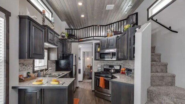 A modern kitchen with dark cabinets, a central island, and a staircase leading to an upper level.