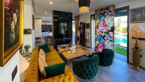 Un salon moderne avec un canapé jaune, des coussins verts, une table basse en bois et un mur décoré d’un motif floral éclatant.