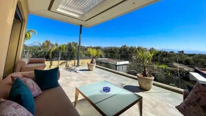 Un balcon moderne avec une table en verre, des sièges confortables et des plantes en pot.