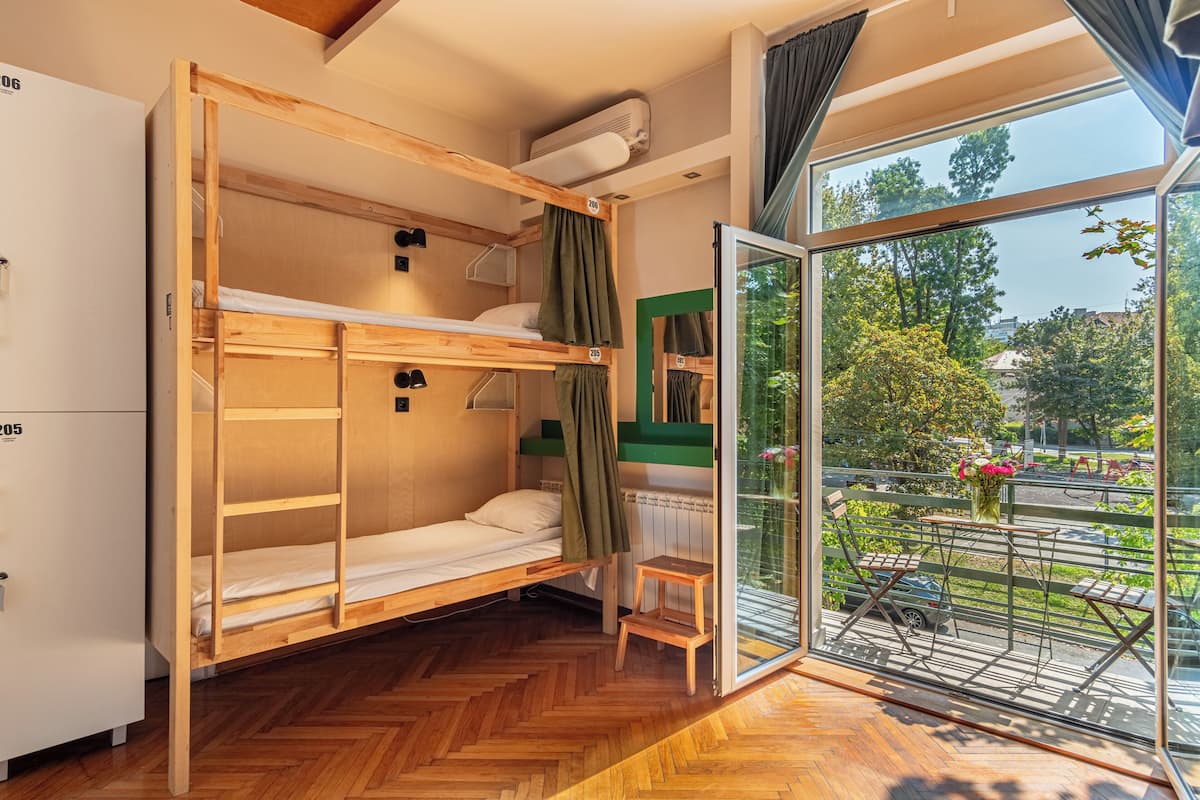 A bunk bed room with a wooden floor, a small table, and a window with a view of a park.
