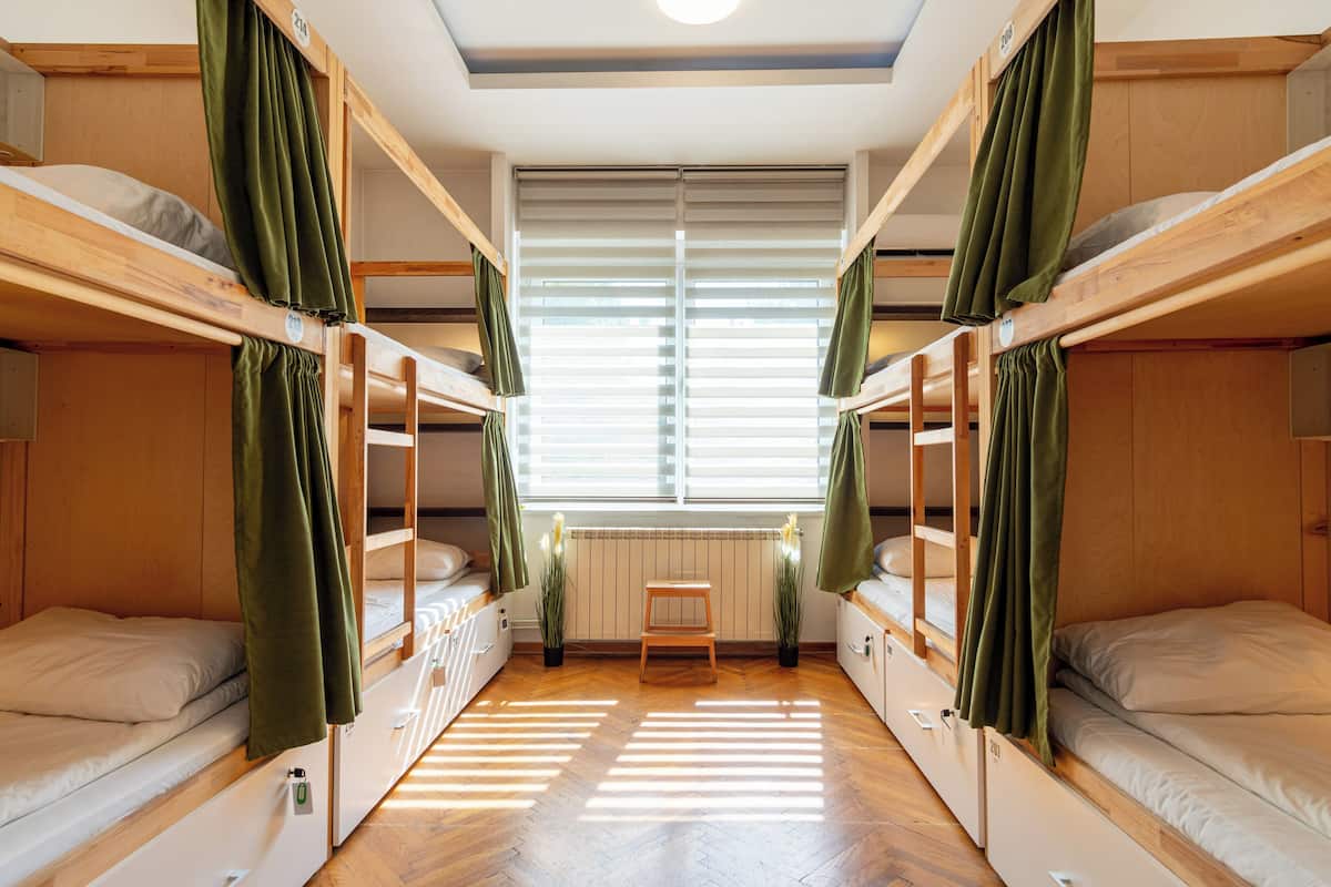 A room with bunk beds, a small table, and a window with blinds.