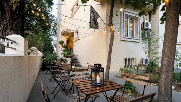 An outdoor seating area with wooden tables and benches, string lights, and potted plants. - Cabbage Hostel (Belgrade)