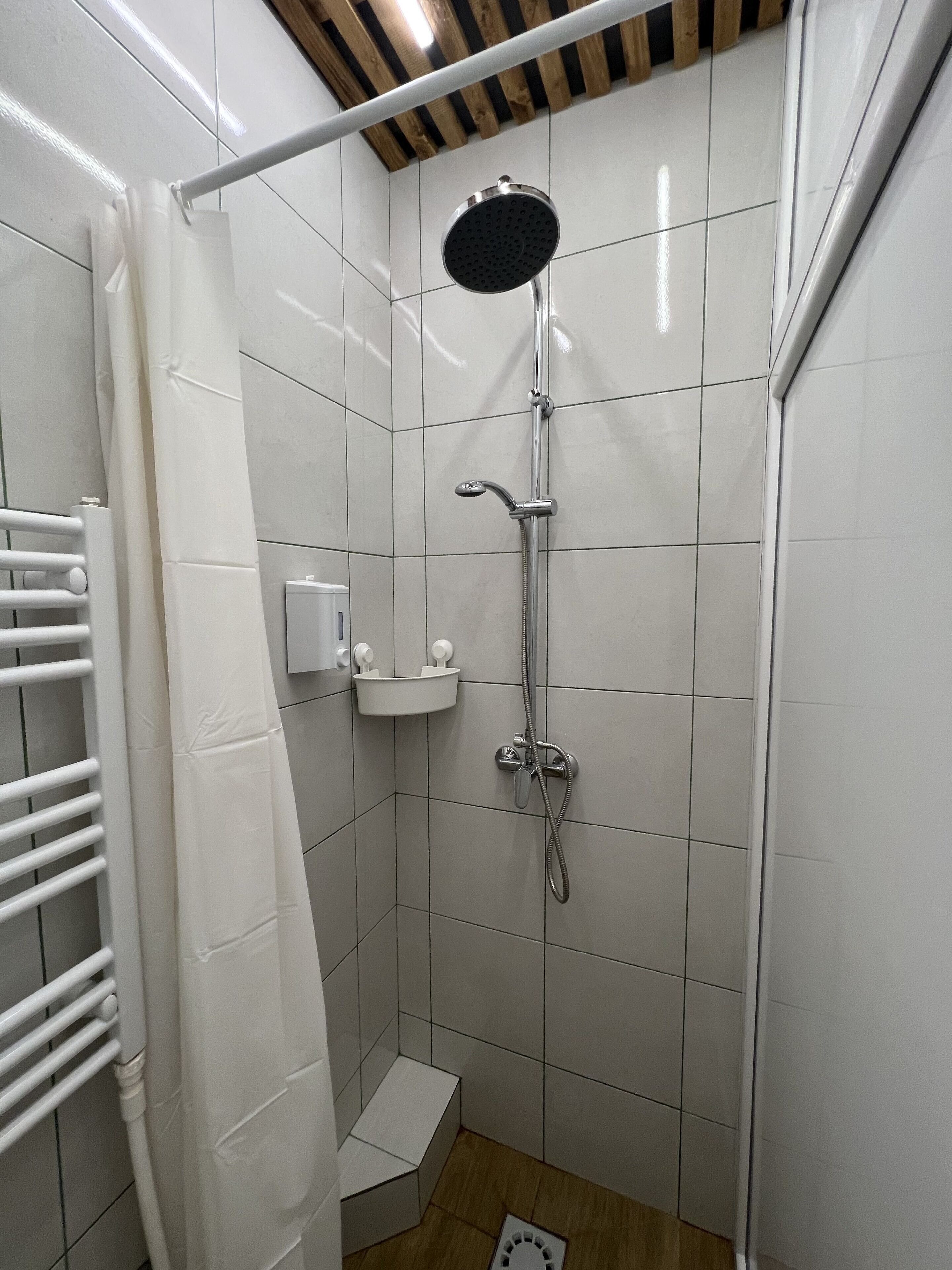 Un pequeño espacio de ducha con azulejos, un cabezal de ducha de mano, un grifo de pared y un estante pequeño con artículos de aseo.