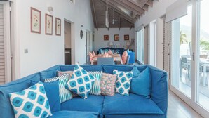 Un canapé bleu agrémenté de coussins à motifs, un coin repas avec une table et des chaises, et une grande porte-fenêtre coulissante donnant sur un espace extérieur.