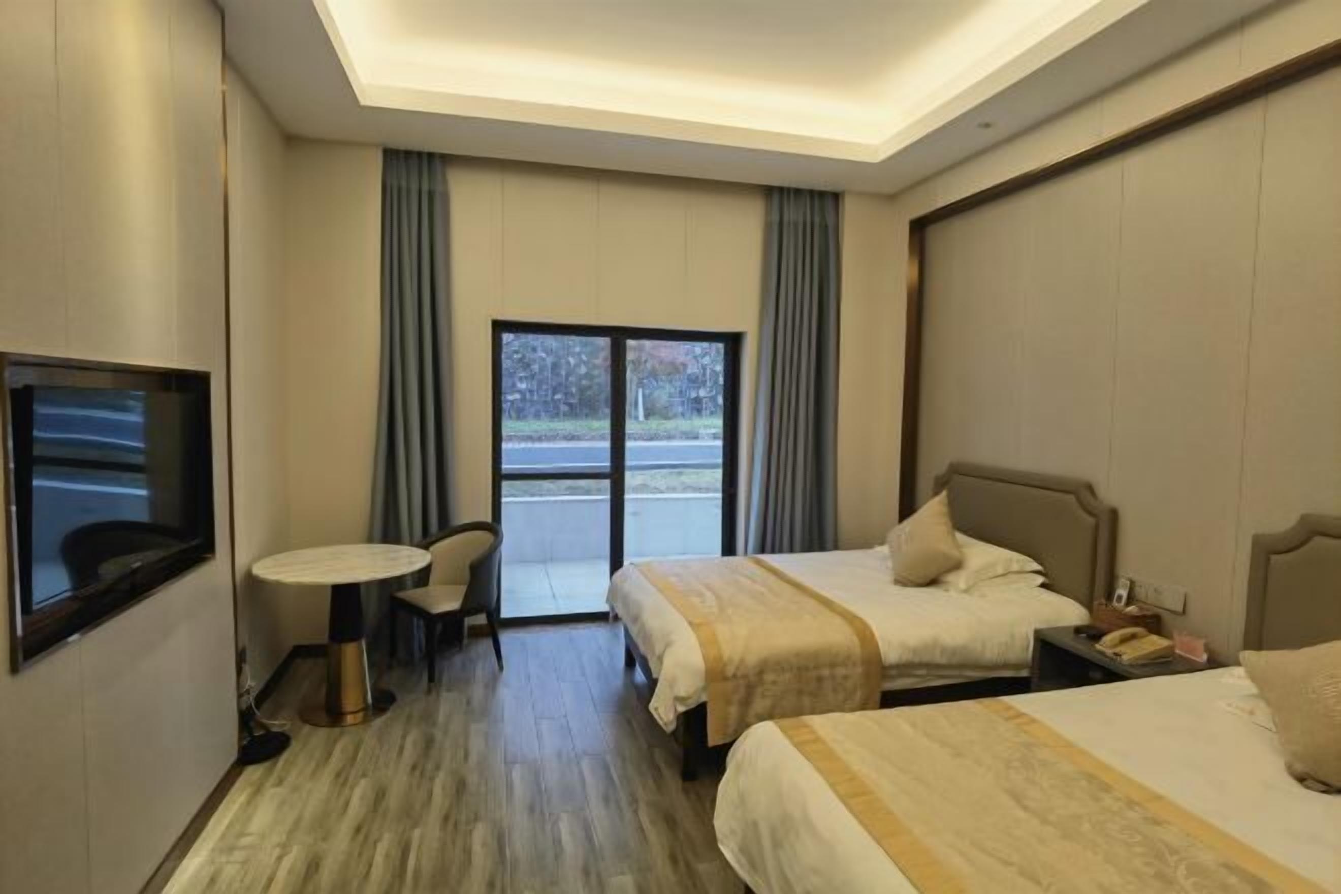 Ein Hotelzimmer mit zwei Betten, einem kleinen Tisch, einem Stuhl, einem Fernseher und Blick ins Freie durch ein großes Fenster.