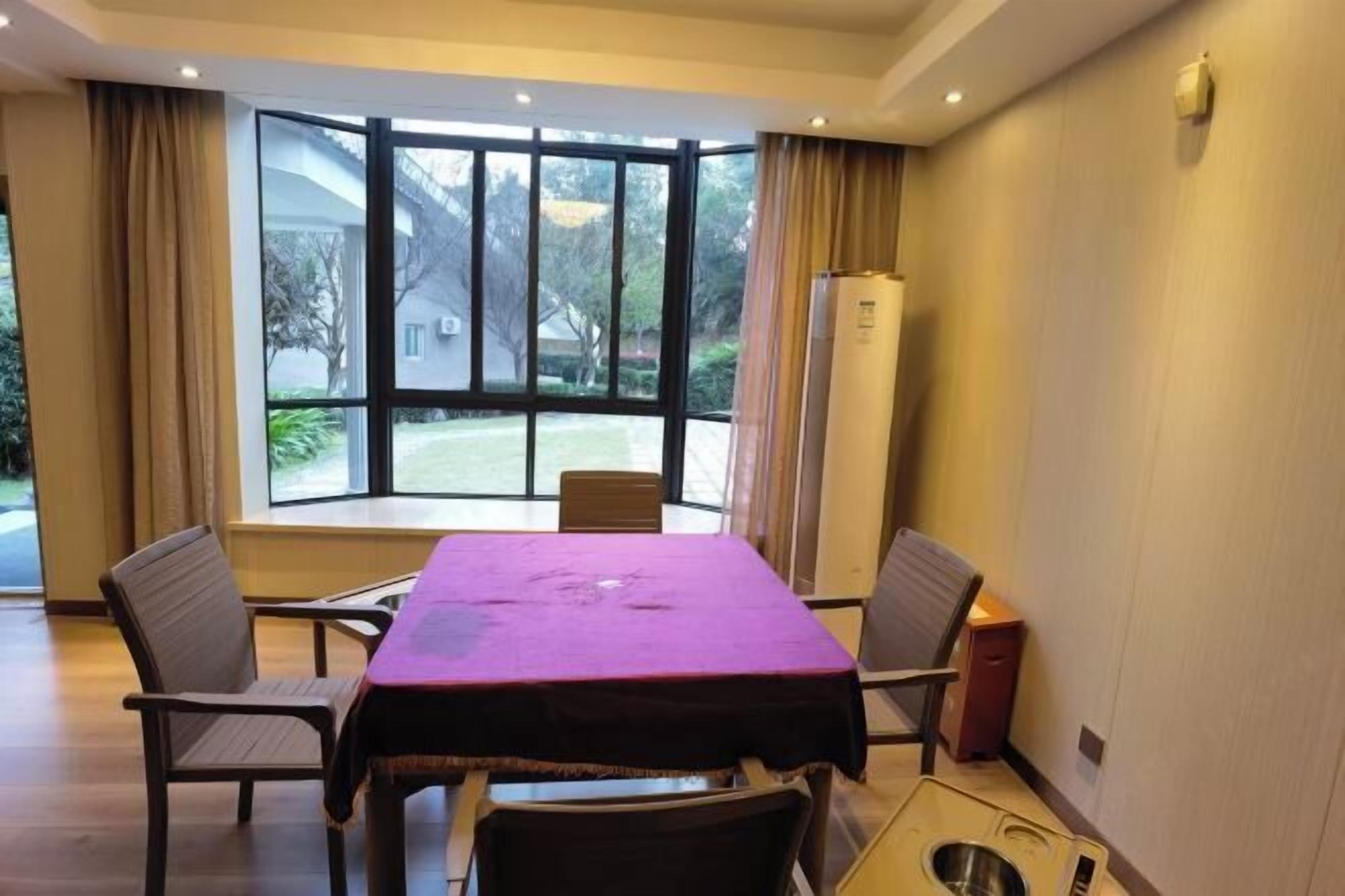 A hotel room with a large window, a table with a purple tablecloth, and a small kitchenette.
