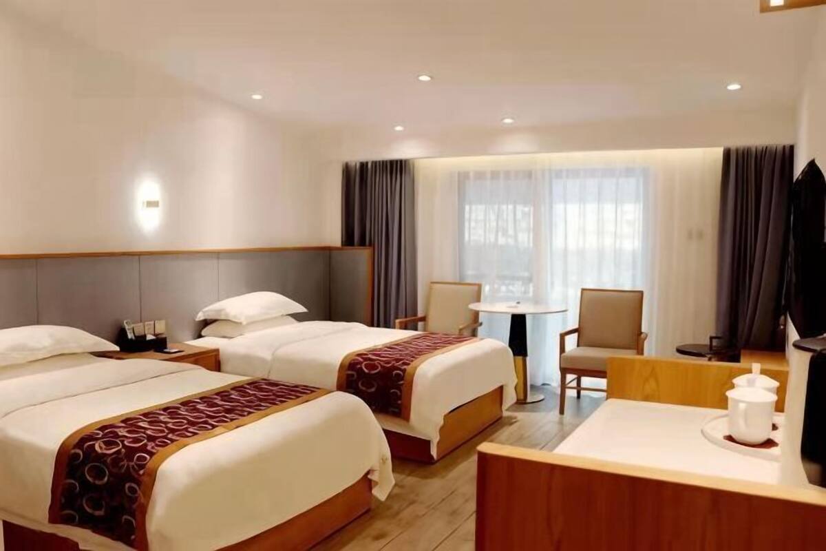 Et hotelværelse med to senge, et skrivebord, en stol, et lille bord og et fjernsyn.
