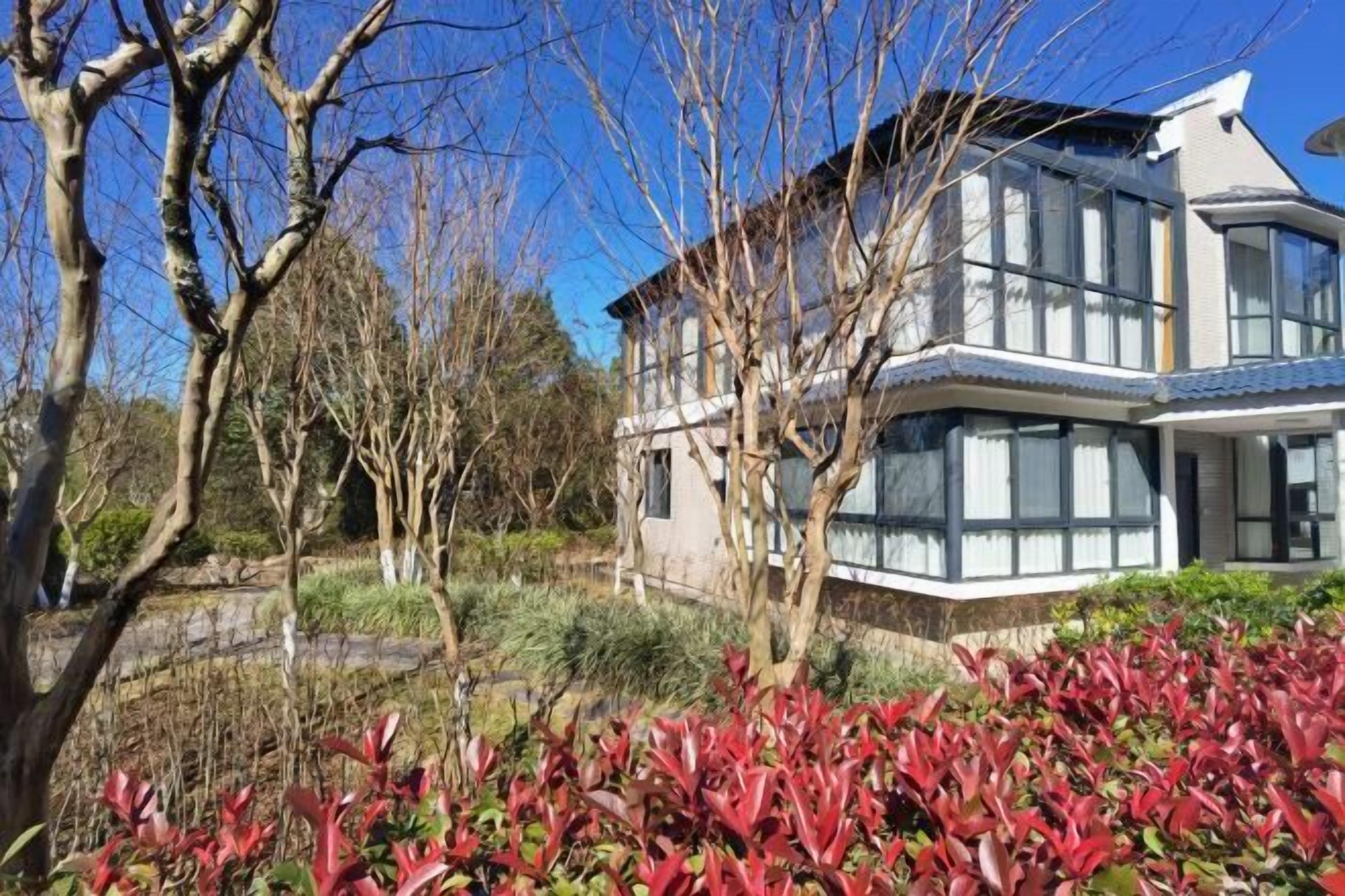 A modern house with a large glass window, surrounded by trees and a garden.
