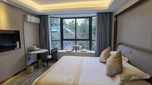 Une chambre d’hôtel moderne avec un grand lit, une petite table, une télévision et une fenêtre donnant sur des arbres.