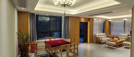 A modern living room with a dining area, featuring a chandelier, wooden furniture, and large windows.