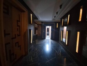 A hallway with a polished marble floor, wooden doors with geometric patterns, and walls with rectangular light fixtures. - Lovely Studio with Terrace in heart of Marrakech (Marrakesh)