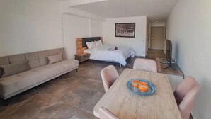 A modern hotel room with a sofa, a wooden dining table with chairs, a bed with a headboard, and a painting on the wall. - Cozy studio with balcony (Marrakesh)